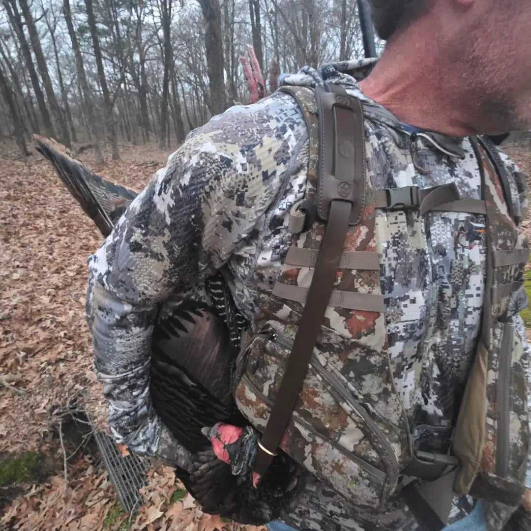 Hunter walking through woods with hands-free turkey tote — bird secured on back