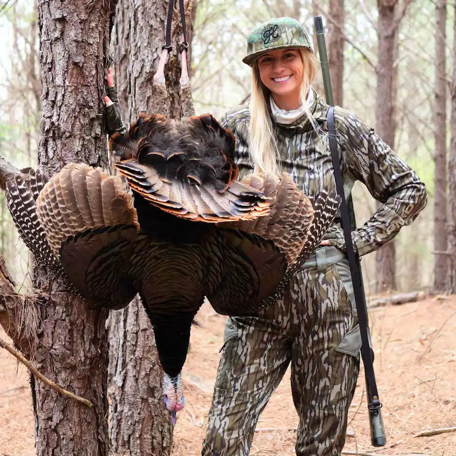 Hunter posing with turkey hanging from tote on tree branch